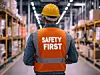 Back view of a warehouse worker wearing a reflective safety vest with “SAFETY FIRST” text, emphasizing industrial safety and workplace protocols.