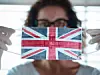 Eine Frau zeigt eine Maske, auf die die Flagge Großbritanniens aufgedruckt ist.