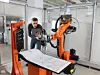 Kuka-Mitarbeiter steht vor Roboterzelle und schaut auf ein Tablet.