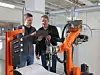 Zwei Kuka-Mitarbeiter stehen vor Roboterzelle und schauen auf ein Tablet.
