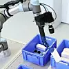 Roboter greift in eine Kiste und entnimmt einen Karton