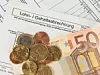 Auf einer Lohnabrechnung liegen ein 50 Euro Schein und mehrere Münzen.