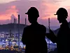 Zwei Arbeiter schauen im Sonnenaufgang auf ein Industriegebiet.