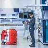 Ein Mitarbeiter steht in einem Werk und navigiert mit einem Tablet ein fahrerloses Transportsystem.