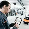Ein Kuka-Mitarbeiter schaut in einem Werk auf ein Tablet und überprüft Daten.