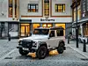 Der klassische Land Rover Defender steht zwischen Häusern in einer Straße.