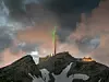 Berggipfel auf mit Bergstation, Hütte, Funkmast und in den Himmel strahlendem grünen Lichtstrahl