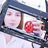 Frau an 3D-Drucker mit additiv gefertigtem Zahnrad aus Kunststoff