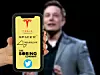 Die Logos von Elon Musks eigenen Unternehmen auf dem Smartphone und Elon Musk im Hintergrund.