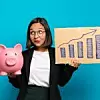 Eine Geschäftsfrau steht vor blauem Hintergrund und hält in der einen Hand ein Sparschwein und in der anderen ein Papier mit einer Statistik darauf.