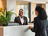 Receptionists at hotel front desk welcoming business people at counter.