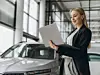 Portrait of confident successful sales woman using laptop computer in car dealership
