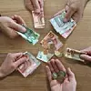 Sechs Hände halten Geld in den Händen und präsentieren dieses.