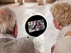 Zwei Senioren schauen zu einem Roboter, auf dem per Video eine Frau und ein Kind zugeschalten sind.