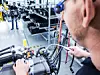 Ein Mann überprüft eine Brennstoffzelle. Im Hintergrund sind weitere Arbeiter des Werkes zu sehen.