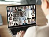 Eine Person schaut auf einen Bildschirm, auf dem eine Online-Videokonferenz mit vielen Teilnehmern zu sehen ist.