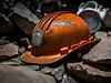 China Mine Disaster 2023: Chinese Mine Collapse Symbolism. Dirty, Dusty Damaged Orange Chinese Hard Hat, Mining Helmet Laying in the Rocks, Debris, and Rubble from a Mine.