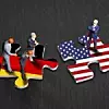 Zwei Puzzleteile, das eine in der Flagge Deutschlands, das andere in der der USA. Auf dem USA-Puzzle steht eine Figur, die wie Donald Trump aussieht. Auf der deutschen stehen drei Menschen.