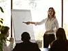 Eine Frau zeigt während einer Konferenz auf eine Grafik, die auf einem Flipchart zu sehen ist.