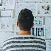 Ein junger Mann schaut auf eine Wand voller Notizen und Post-Its.