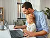 Ein Mann arbeitet mit seiner Tochter auf dem Schoß im Homeoffice