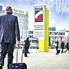 Mann mit schwarzem Anzug und Rollkoffer vor Motek Messegebäude