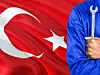Türkischer Mechaniker in blauer Uniform hält Schraubenschlüssel, dahinter eine wehende Türkei-Flagge