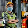 Arbeiterin trägt Mundschutz, eine Warnweste, einen Helm und eine Schutzbrille.