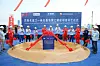 Spatenstich-Zeremonie in Zhanjing China, BASF-Werk. Leute mit Schutzhelmen stehen im Kreis um einen Krater aus Sand mit einer geschmückten Infotafel darin und klatschen.