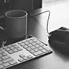tastatur, tasse und Maus auf einem Tisch an dem gearbeitet wird