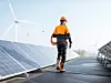 Monteur geht zwischen Photovoltaikanlage - im Hintergrund Windkraftanlagen