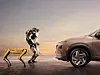 Zwei Roboter von Boston Dynamics stehen einem Hyundai-Fahrzeug gegenüber.