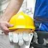 Eine Person hält einen gelben Helm und Arbeitshandschuhe.