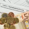 Auf einer Lohnabrechnung liegen ein 50 Euro Schein und mehrere Münzen.