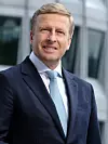 Portrait von Oliver Zipse, Vorstandsvorsitzender BMW; lächelnder Mann mit blonden Haaren, er trägt einen dunkelblauen Anzug mit weißem Hemd und hellblauer Krawatte