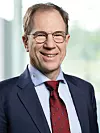 Portrait von Reinhard Ploss, CEO Infineon; lächelnder Mann mit braunen Haaren und ovaler Brille, trägt eine dunkelblaues Jackett mit hellem Hemd und roter Krawatte