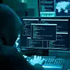 Hacker in dunklem Kapuzenpulli vor mehreren Bildschirmen