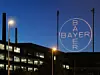 Nächtliche Szene: beleuchtetes Logo des Bayer-Konzern vor dunklem Gebäude