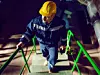 Ein Mann in blauem Schutzanzug und gelben Helm geht eine Treppe nach oben.