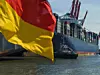Containerschiff legt am Hafen an. Im Vordergrund weht eine Deutschlandflagge.