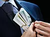 Ein Mann im Anzug schiebt sich Geld in die eigene Tasche