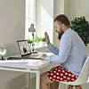 Ein Mann sitzt mit Hemd und einer gepunkteten roten Hose vor einem Laptop und winkt seinem Gesprächspartner, der online zugeschaltet ist, zu.