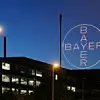 Nächtliche Szene: beleuchtetes Logo des Bayer-Konzern vor dunklem Gebäude
