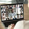 Eine Person schaut auf einen Bildschirm, auf dem eine Online-Videokonferenz mit vielen Teilnehmern zu sehen ist.