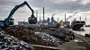 Symbolbild eines Schrottplatzes mit Stahlrecycling, Greifbagger, Stahlwerk und Frachtschiff im Hafen.