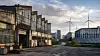 Ältere Industriehalle neben modernen Gewerbebauten, Solarpaneelen und Windrädern als Symbol für den Rückgang industrieller Betriebe in Deutschland.
