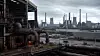 Symbolbild einer energieintensiven Industrieanlage mit Rohrleitungen, Schornsteinen und Kühltürmen unter grauem Himmel.