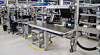 Moderne Produktionslinie mit Metalltischen, Monitoren und Fördertechnik in einer Industriehalle.