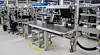 Moderne Produktionslinie mit Metalltischen, Monitoren und Fördertechnik in einer Industriehalle.