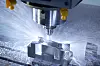 CNC-Fräskopf bearbeitet ein Metallteil mit Kühlmittelstrahl in einer Werkstatt.